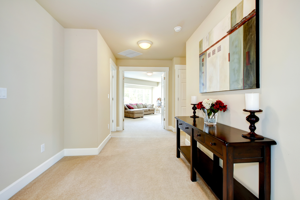 Large home hallway with art and furniture, beige carpet.