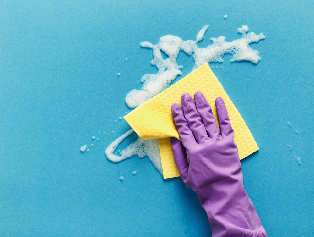 Cleaning concept - hand in orange protective rubber glove washing glass window with rag and detergent foam. Householding background, copy space